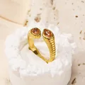 Détail d'une bague spirale dorée avec zircons orange sur un socle en pierre blanche - Pierre Champagne Or