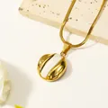 Nahaufnahme der goldenen Schlangenkette mit rundem weißen Muschel-Anhänger auf Stein - Gold Weiß Emaille