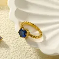Detailopname van de vergulde ring met blauwe edelsteen en kralentextuur in een schaaltje - Goud Blauwe Zirkonia