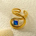 Detailansicht vergoldeter Spiralring mit blauem Zirkon auf sandigem Hintergrund - Einstellbar Offen / Vergoldet Blauer Zirkonia
