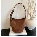 Detail view of brown suede bucket bag featuring woven handle and round coin purse charm - Coffee