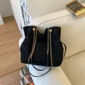 Black suede hobo bag with gold chain straps and drawstring detail on white sofa - Black