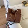 Dark coffee suede bucket bag with gold chain strap and drawstring detail on sofa - Brown