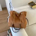 Brown suede tote bag with golden chain strap and drawstring design on a white sofa - Brown