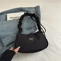 Black crescent underarm bag with silver bow detail and pleated handle on denim background - Black
