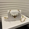 Minibolso tejido blanco con asa de perlas y cierre de corazón dorado sobre un libro - Blanco