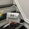 Silver sequin handbag with bow detail and metallic flap, shown in hand for style - Silver