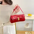 Glossy red patent leather shoulder bag with gold clasp shown in a lifestyle cafe setting - Red