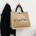 Linen mama tote bag with black handles and heart print shown hanging on a wooden wall hook - Black