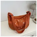 Detail of orange corduroy crescent bag featuring white embroidered letters and wide strap - Orange