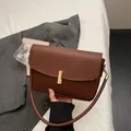 Bolso pequeño cuadrado marrón oscuro minimalista con hebilla dorada y textura de cuero - café