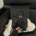 Black shell handbag with golden hardware and matching mini pouch on a white cloth background - Black