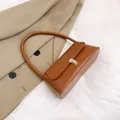 Karamellbraune Baguette-Tasche mit goldenem Schloss auf beigefarbenem Trenchcoat - Braun