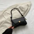 Matte black underarm bag with gold clasp and knotted strap on a white blazer - Black