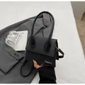 Minimalist black trapezoid handbag with a large arched handle and matte leather finish - Black