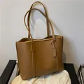 Minimalist brown soft leather tote bag with dual straps and decorative tag detail - Brown