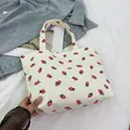 Close-up of white corduroy tote bag featuring red strawberry print and sturdy dual handles - Off White