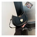 Elegant black crescent saddle bag featuring a distinctive golden heart-shaped metal clasp - Black
