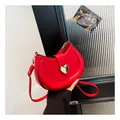 Red saddle bag with golden heart buckle and slim shoulder strap held by hand - Red