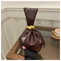 Minimalist dark brown pleated bucket bag with gold metal handle in a cozy cafe setting - Brown