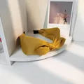 Nahaufnahme eines ingwerfarbenen Stirnbands mit Knotendesign auf einem weißen Regal - Gelb