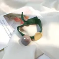 Detail eines waldgrünen Haargummis mit goldener Metallscheibe und glänzender Acrylperle - Grünes Gummiband