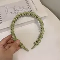 Detalle de diadema de satén verde claro plisada con una textura suave de acabado sedoso - Verde