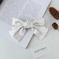 Elegante crèmewitte satijnen strik haarklem op een boek voor een zachte, esthetische look - Melkgrijs