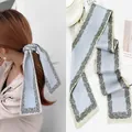 Detail view of light blue silk scarf featuring vintage patterns used as a hair tie and headband - Blue With Lace Border