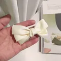 Elegante fermaglio per capelli con fiocco a triplo strato color crema mostrato a mano - Beige