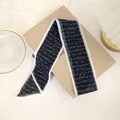 Detail eines schwarz-weißen Chiffon-Haarbandes mit elegantem Buchstabendruck auf Box - Alphabet-Aufkleber mit schwarzem Hintergrund