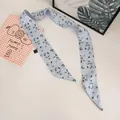 Close-up of a light blue floral twilly silk scarf with white flower patterns and washing label - Light Blue