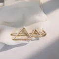 Dettaglio di un fermaglio geometrico dorato con perle su elegante sfondo in chiffon bianco - Triangolo
