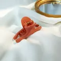 Detail of glossy coral orange hair claw clip with golden spring on white fabric - Pink