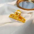 Close-up of a glossy yellow hair claw clip on white fabric with a decorative gold mirror - Yellow