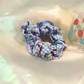 Detailed view of blue plaid scrunchie with red cherry patterns on soft textured cloth - Blue