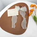 Detailed view of white organza bow hair tie with long ribbons on brown leather mat - White