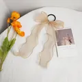Detail of beige organza bow hair tie with long ribbons on white textured fabric - Yellow