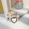 Detail eines beigen Satin-Haargummis mit einem schwarz umrandeten weißen Herz-Anhänger - Groß / Beige