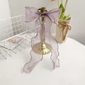 Detail view of light purple organza bow scrunchie with long ribbons on a gold stand - Purple