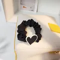 Nahaufnahme eines schwarzen Scrunchies mit Herzanhänger auf einer weißen Tasche - Klein / Schwarz