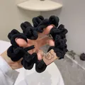 Close-up of black plush scrunchie with soft pleated texture and small bear label - Black