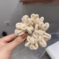 Close-up of cream plush scrunchie made of thick chenille fabric with a designer tag - Cream