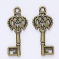 Pair of vintage bronze alloy key pendants with ornate hollow carvings on white background - Antique Bronze