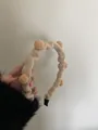 Detalle de diadema de punto beige con pompones que muestra textura acanalada y puntas - Caqui