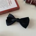 Detail of multi-layered black satin bow hair clip on a warm aesthetic background - Black