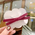 Hand holding a burgundy grosgrain bow hair clip on a cloud card in a cafe setting - Purple