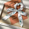 Dettaglio di uno scrunchie floreale con nastri e stampe di foglie verde su seta bianca - Base Bianca