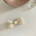 Elegante horquilla de lazo plisado crema con detalles de perlas en fondo minimalista - Estilo de lazo con borde ondulado