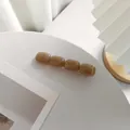 Détail d'une pince à cheveux en résine ambrée à texture marbrée sur un plat blanc - Café Clair